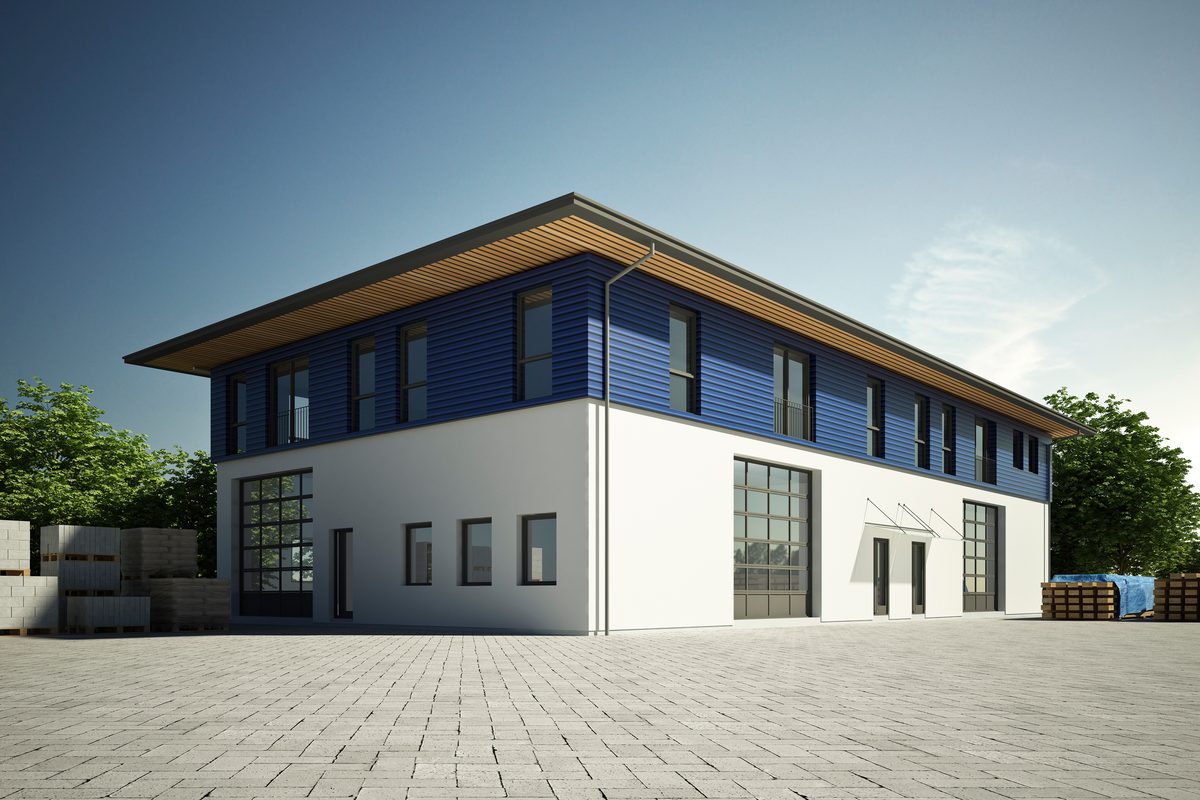 Zweigeschossiges Betriebsgebäude mit Rolltoren und blau verschaltem Obergeschoss, davor ein gepflasterter Hof mit Paletten