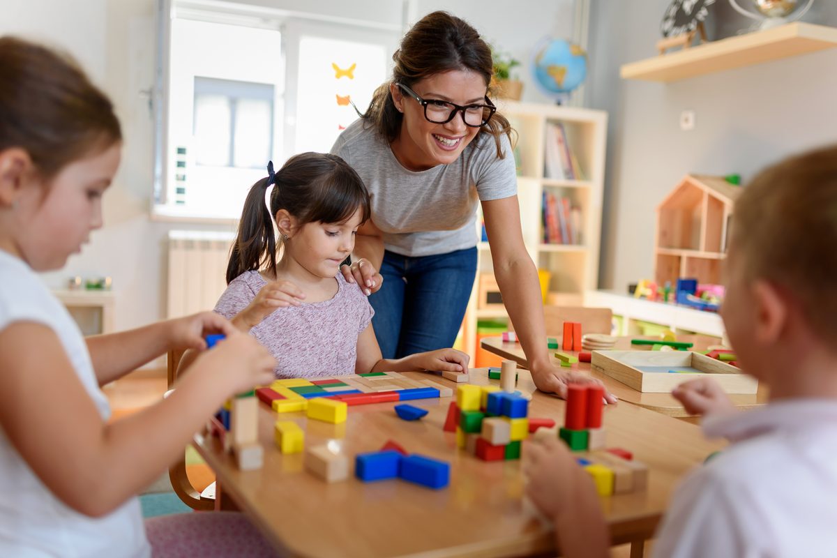 Erzieherin und drei Kinder bauen gemeinsam mit Holzbausteinen an einem Tisch
